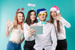© Elizaveta - New Year theme Christmas winter office company employees. Group 4 young Caucasian people business smile holiday funny hats accessories glasses take photo yourself selfie tablet blued background.