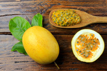 Pulp Of Passion Fruit In The Wooden Spoon Next To Passion Fruit Cut In Half And Whole On Wooden Table