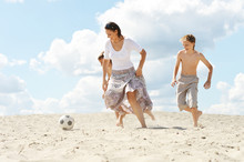 Portrait Of Happy Family Playing Football On Beach In Summer Day