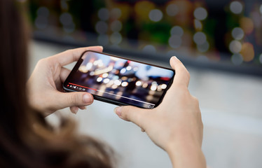 Cropped image of woman hand holding smartphone and watching video with night bokeh background.