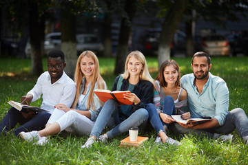 group of young students sitting together on green lawn high school university campus