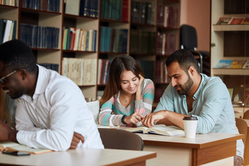 Group of concentrated multiracial diverse students reading books, drinking coffee and preparing to exam in library. People, knowledge, education and professional orientation concept