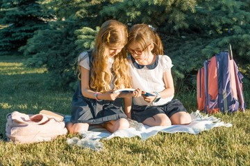 two little girl friends schoolgirl learning sitting on a meadow in the park. children with backpacks