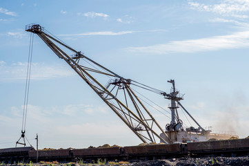 Wall Mural - A huge excavator overloads in the dumps rock from the unloaded train from the mine against a clear blue sky. Concept: mining and environmental problems