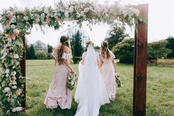 Bridesmaids in pink dresses with a bunch of flowers. Girl with a bouquet of flowers at the wedding ceremony. Wedding Arch