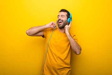 Wall Mural - Man on isolated vibrant yellow color listening to music with headphones