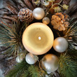 Ein Weihnachtsgesteck mit großer brennender Kerze. Umrahmt von Tannenzapfen und Nadelzweigen. Weiße und silberne Weihnachtskugeln veredeln das Gesteck