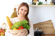 © rogerphoto - Young happy woman holding paper bag full of vegetables and fruits while smiling. Girl have made shopping and ready for cooking  in kitchen