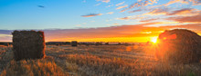 Panoramic View Of Hay Bales On The Field After Harvesting Illuminated By The Last Rays Of Setting Sun