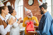 © pressmaster - Two happy businesswomen clapping their hands while young man giving birthday present to senior boss
