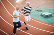 © pressmaster - Two friendly men in activewear running down sport tracks on modern stadium and chatting on the move
