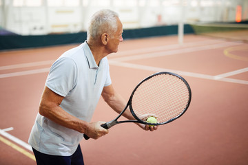 Wall Mural - Aged tennis player in activewear holding racket and ball while aiming at his opposite during game