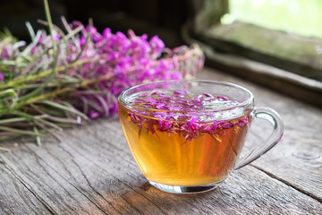 Wall Mural - Fireweed healthy herbal tea. Mug of chamerion tea and bunch of medicinal herbs on background inside the retro village house.