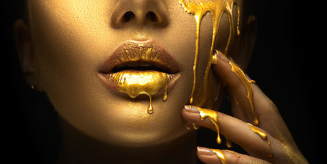 Poster - Golden paint smudges drips from the face lips and hand, golden liquid drops on beautiful model girl's mouth, creative abstract makeup. Beauty woman face