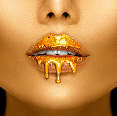 Poster - Gold paint drips from the sexy lips, golden liquid drops on beautiful model girl's mouth, creative abstract makeup. Beauty woman face