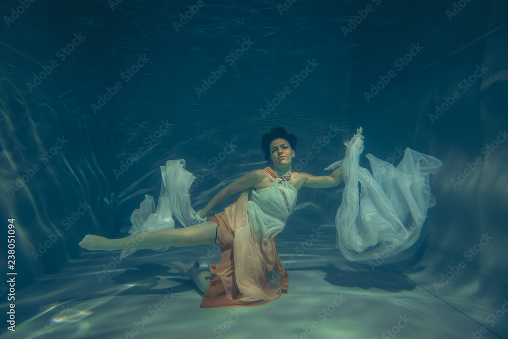 elegant slender girl swims underwater like a free diver in a white evening dress with beautiful fabric - obrazy, fototapety, plakaty 