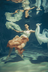 Wall Mural - elegant slender girl swims underwater like a free diver in a white evening dress with beautiful fabric