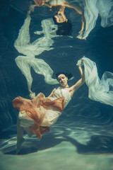 Wall Mural - elegant slender girl swims underwater like a free diver in a white evening dress with beautiful fabric