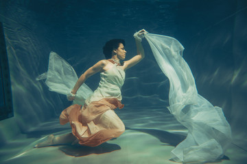 Wall Mural - elegant slender girl swims underwater like a free diver in a white evening dress with beautiful fabric