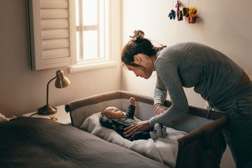 Wall Mural - Young mother looking at her baby sleeping in a crib