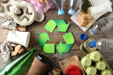 Recycling symbol and different garbage on wooden background, top view