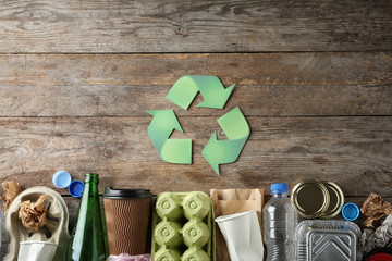 Recycling symbol and different garbage on wooden background, top view