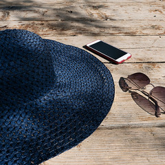 Blue straw hat, sunglasses and phone on wooden boards.