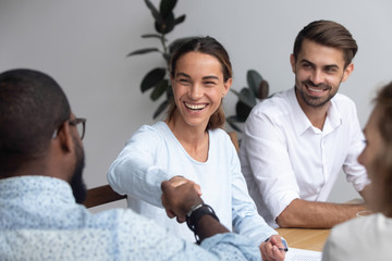 Poster - Attractive young mixed race woman shaking hands with black partner starting negotiations sitting together in office boardroom with colleagues company members millennial staff feels good and satisfied.