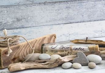 Nautical still life with old I love you message in a bottle, stone heart and driftwood