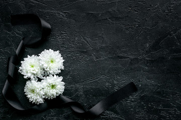 Wall Mural - Funeral symbols. White flower near black ribbon on black background top view space for text