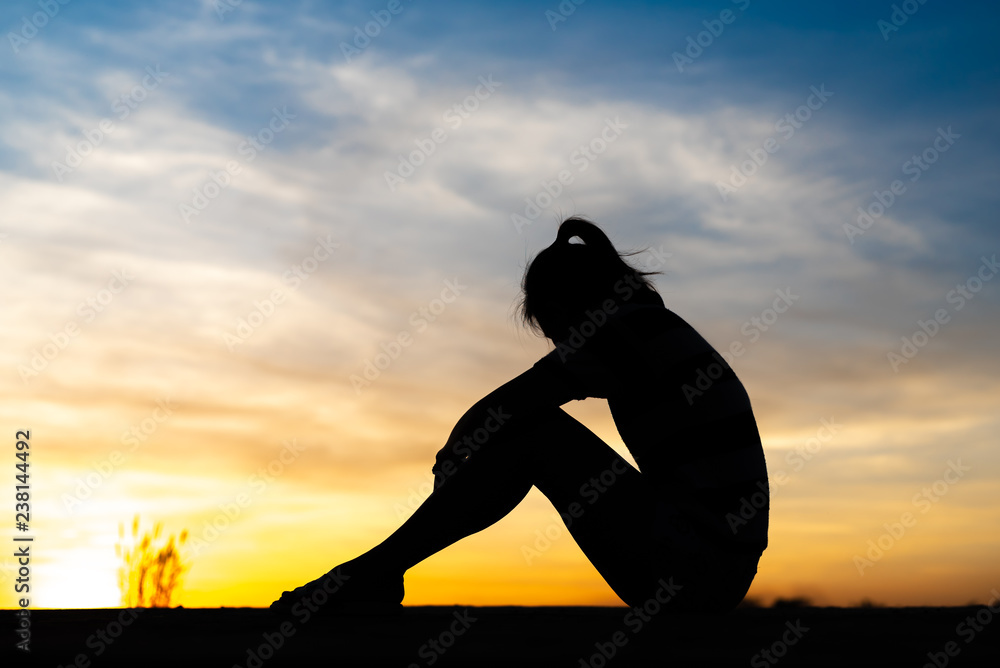Silhouette woman sitting sad in the sunset. Stock Photo | Adobe Stock