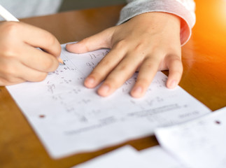 Close up kid's hand writing on paper, writing messy math on wooden table in room,student child girl holding pen doing homework at home, calculate the results on paper , education concept