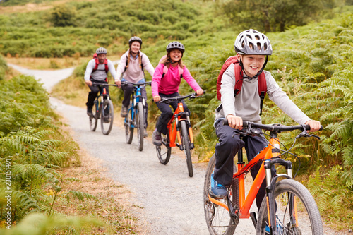 Cuadros en Lienzo Pre-teen boy riding mountain bike with his sister and parents during a family ca