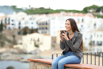 Wall Mural - Happy woman on a ledge drinking and looking away