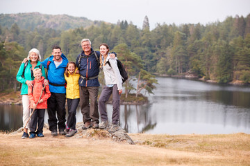 multi generation family stand embracing by a lake, smiling to camera, front view, lake district, uk