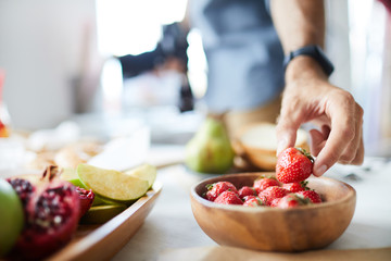 Closeup of unrecognizable photographer holding single strawberry while doing food-photography in studio, copy space