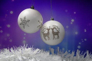 Two white Christmas balls with snowflake and reindeer in front of purple blue background.Christmas still life .Two Christmas balls hanging in front of a blue purple wall.