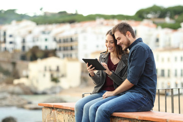 Sticker - Couple sitting on a ledge using a tablet on vacation