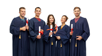 Wall Mural - education, graduation and people concept - group of happy graduate students in mortar boards and bachelor gowns with diplomas over white background