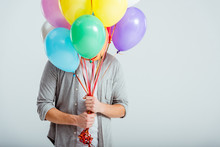 Man In Grey Clothes Hiding Behind Bundle Of Colorful Balloons With Copy Space On Grey Background