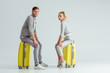 beautiful couple sitting on suitcases and looking at camera on grey background, travel concept