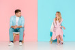 © LIGHTFIELD STUDIOS - man with folded hands sitting on chair and looking at bored woman touching chin on pink and blue background