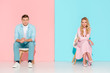 couple with folded hands sitting on chairs and looking at camera on pink and blue background
