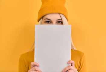 Indoor closeup monochrome portrait of of cheerful woman covers face with white book, has joyful expression, blank copy space for your advertising or promotional text, isolated on yellow background.