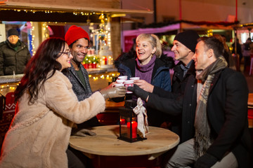 Wall Mural - Group of friends cheering with traditional drink at Christmas market.