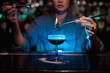 Girl adding to a brown cocktail a flamed badian with tweezers in the blue light