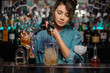 Girl pouring to the measuring glass cup with ice cubes an alcoholic drink from jigger