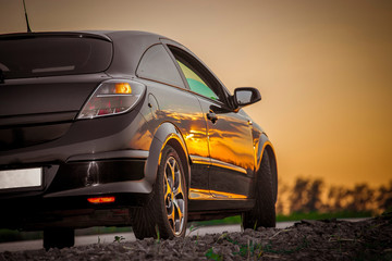 beautiful black modern car stands on asphalt road in summer illuminated by the rays of the sunset