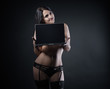 © Vitte Yevhen - Sexy young brunette woman in black sensual lingerie using laptop and posing on black background wall in studio.