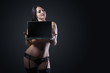 © Vitte Yevhen - Sexy young brunette woman in black sensual lingerie using laptop and posing on black background wall in studio.